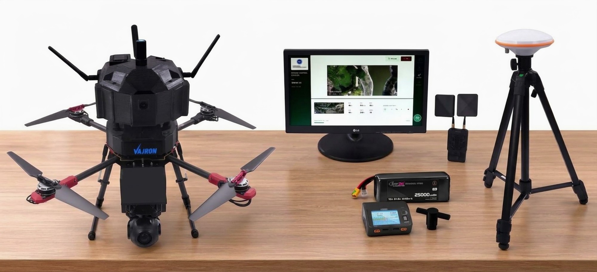 System kit on a table: the VAJRON aircraft, a ground station display, an RTK base antenna on a tripod, a battery and charger.